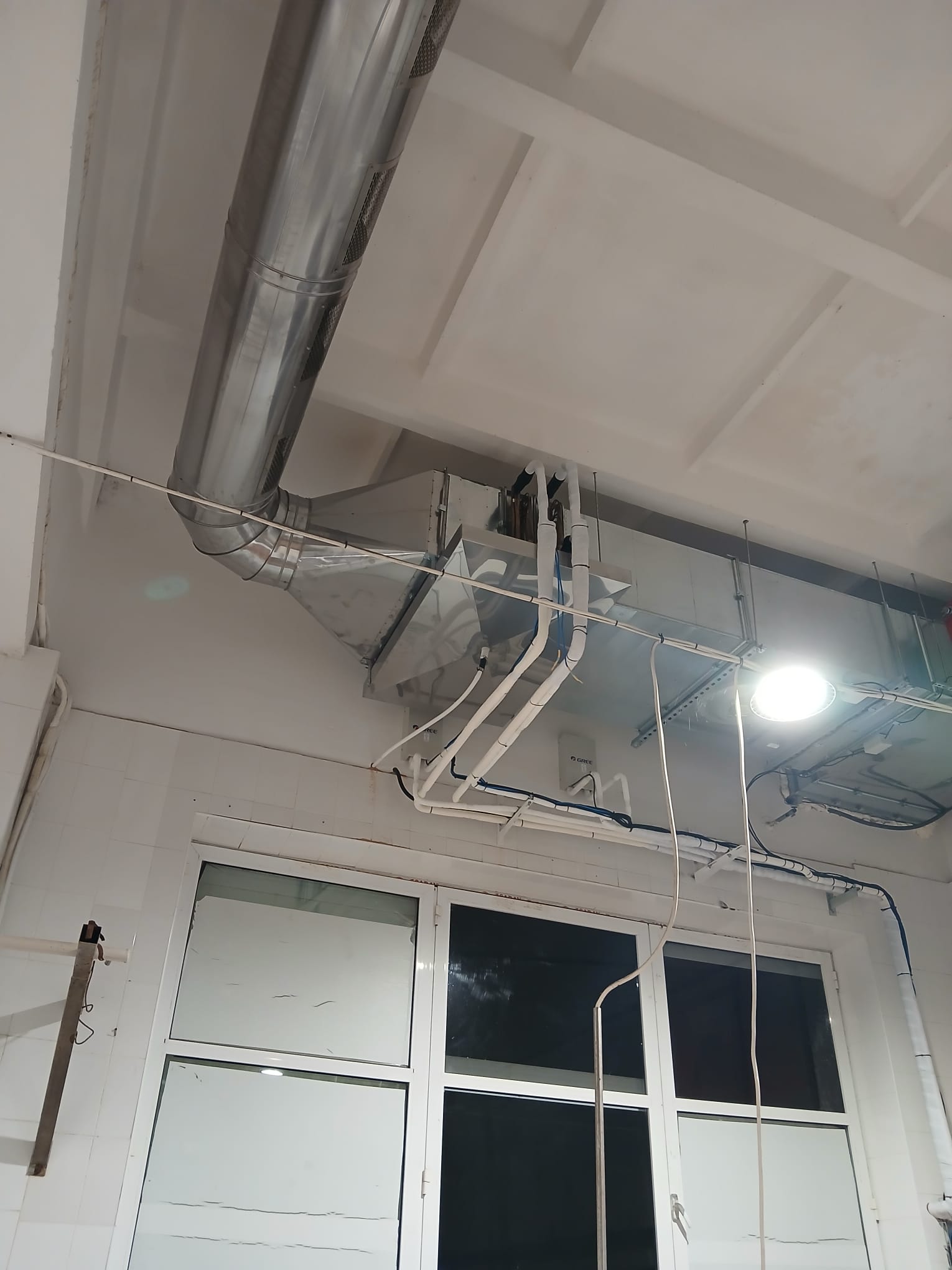 Sistem de ventilație industrială instalat pe tavan, cu conducte metalice, hotă de captare și traseu tehnic pentru evacuarea aerului.