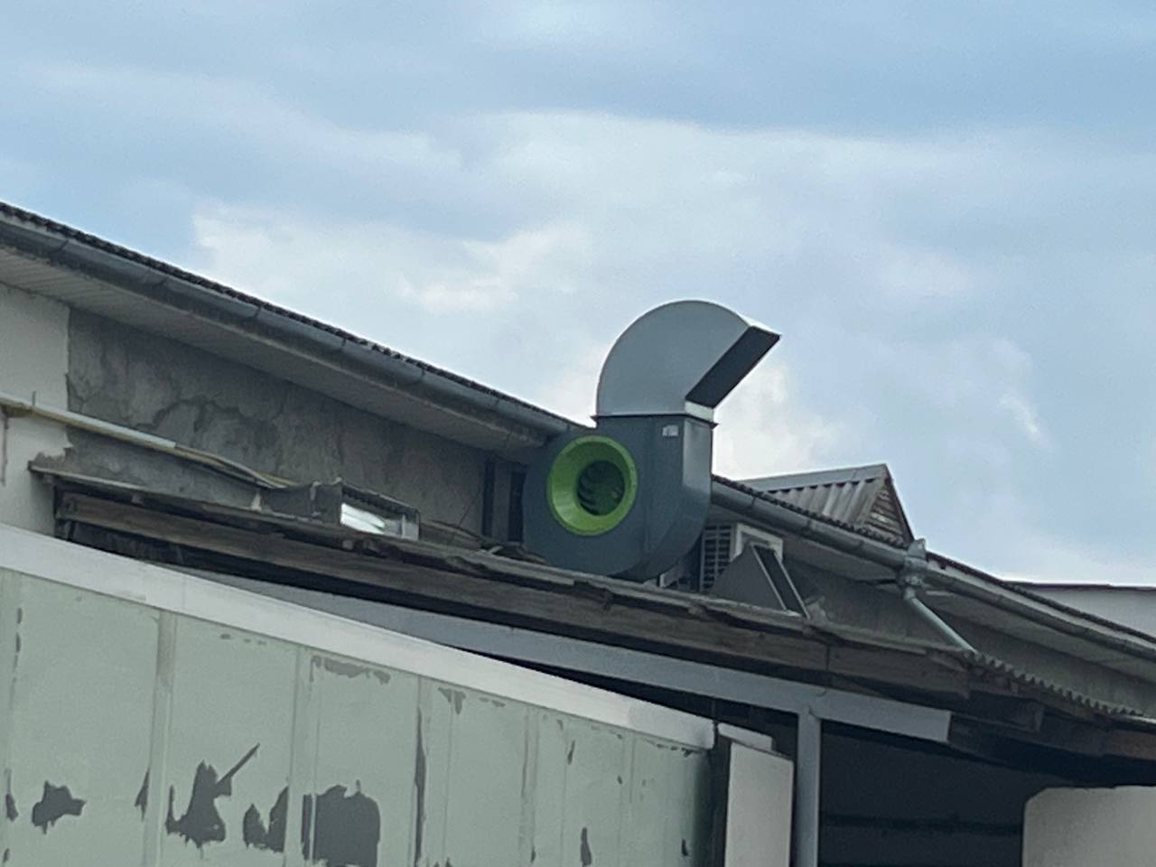 Ventilator industrial montat pe acoperiș, conectat la sistemul de evacuare a aerului pentru o clădire comercială sau de producție.